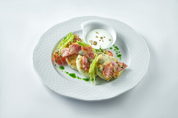 Delicious breakfast - salted cheesecakes with bacon and sour cream in a white plate on a white background. Syrniki