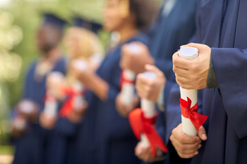 education, graduation and people concept - group of happy international graduate students in mortar boards and bachelor gowns with diplomas