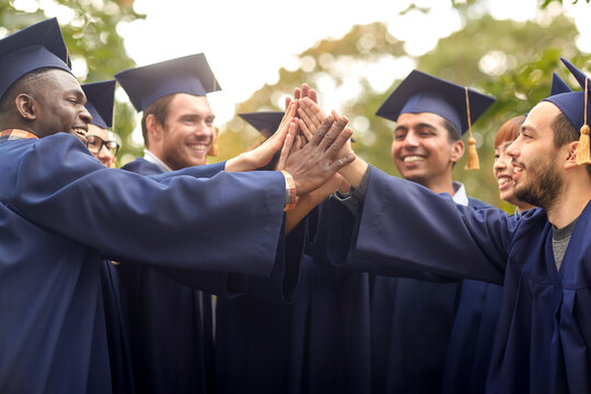 education, graduation and people concept - group of happy international graduate students in mortar boards and bachelor gowns making high five