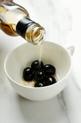 Black olives in the white cup, pouring fresh delicious olive oil