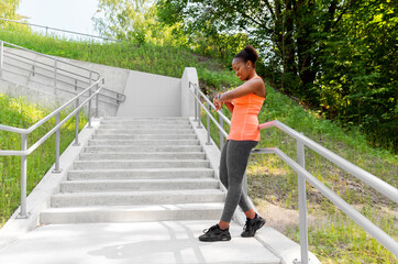 Obraz premium technology, sport and people concept - happy smiling young african american woman with fitness tracker outdoors