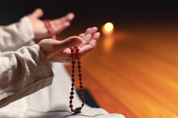 close-up of a male practitioner's hand sitting in lotus position in a dark meditation room with a rosary in his hands