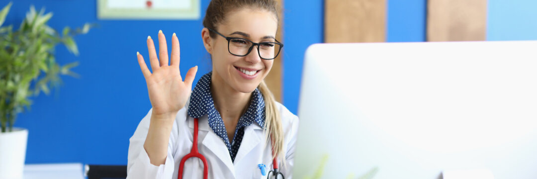 Portrait Of Smiling Doctor Greeting And Waving Hand. Practitioner Giving Online Consultation. Lady Looking At Computer With Gladness. Healthcare And Online Medicine Concept