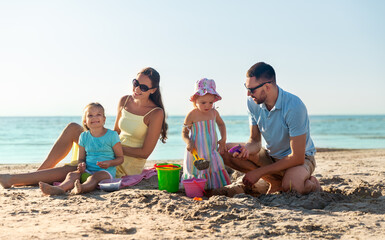 family and leisure concept - happy father, mother and daughters on summer beach