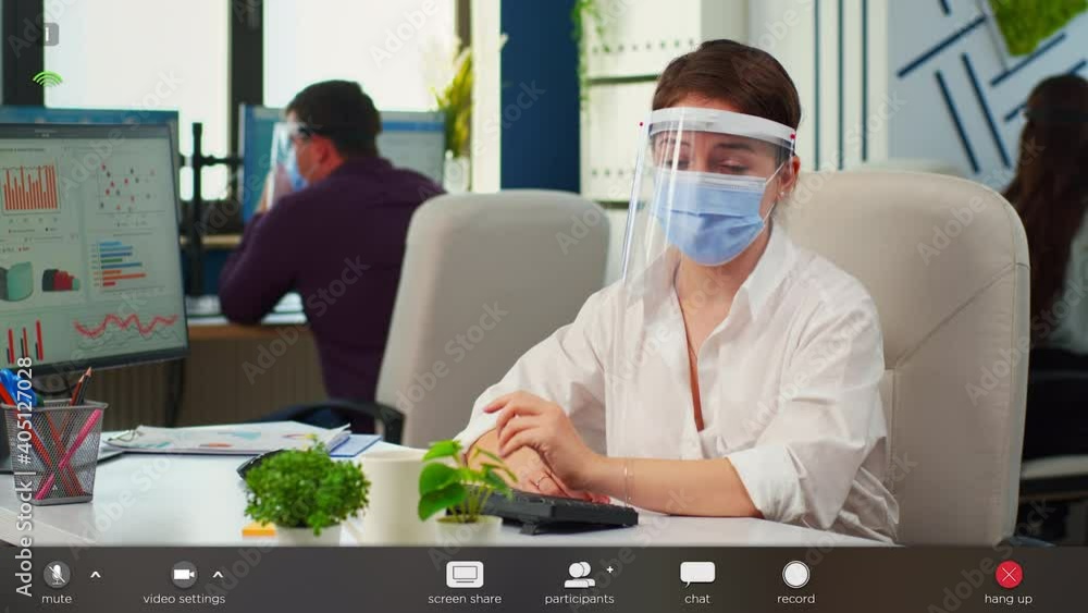 Poster businesswoman with visor and mask talking in front of camera having video call with partners. pov of