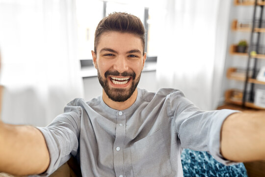 technology, people and lifestyle concept - happy man taking selfie or having video call at home