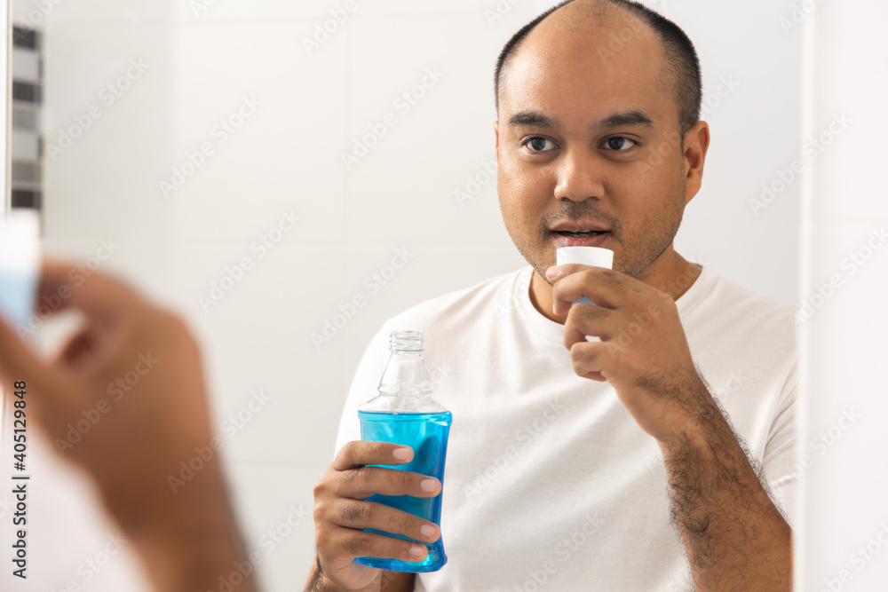 Wall mural young man is gargling with a blue mouthwash. for good dental health and fresh bad breath