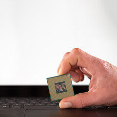 Hand holding cpu processor against keyboard and white