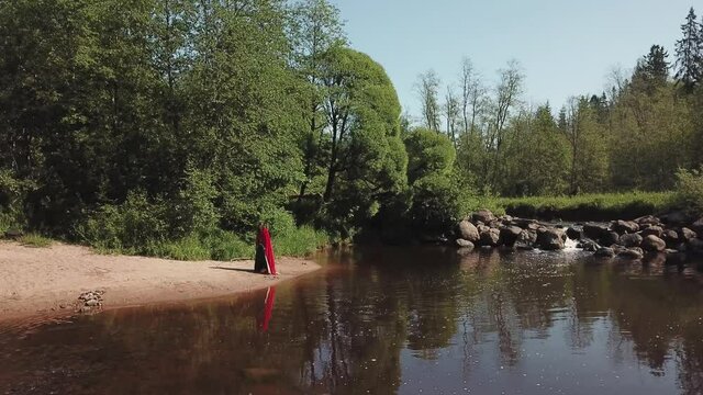 A girl in a red cloak walks on the sand, along the shore along the sandy beach, on the banks of the river with a beautiful waterfall. Aerial photography. Shooting from a quadrocopter, drone.