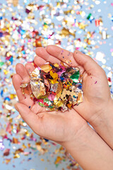 A woman holds sparkles of confetti in her palms on a blue background.