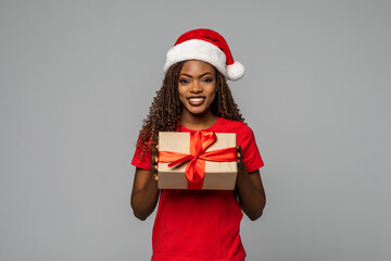 Young African American woman wearing a santa hat opening a gift box on white background