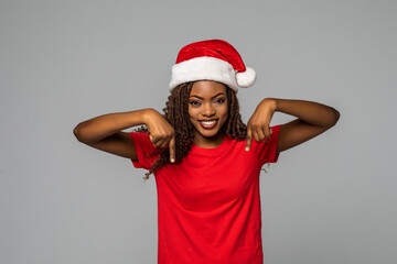 Beautiful african woman in santa hat pointed down on grey background