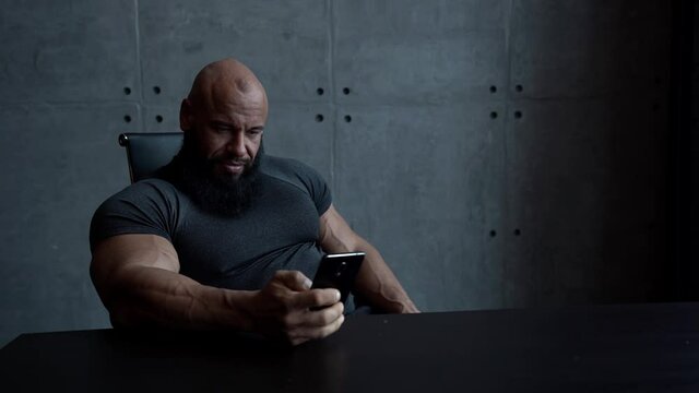 muscular man is using smartphone in room, sitting at table, checking email