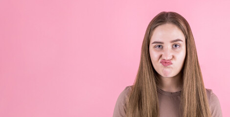 girl looks at the camera with a dubious and indecisive expression on her face, chasing her lips as if she is forbidden to say something. Confused young woman posing isolated on pink wall