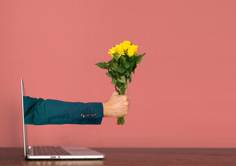 Hand coming out of a laptop with yellow roses in hand. Valentine's day Covid Concept.