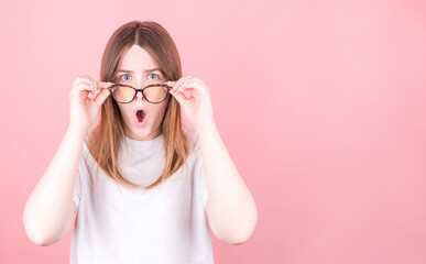 Young woman wearing glasses is very surprised looking at the camera and lowering her glasses....