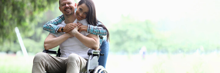 Portrait of happy sweet couple spending time together in nature. Attractive woman embrace man and smiling on camera. Cheerful people in park. Happiness and disabled people concept