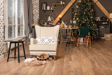 Cozy home interior. An armchair with a table and a small warm rug with slippers and a basket with Christmas tree decorations in the living room.