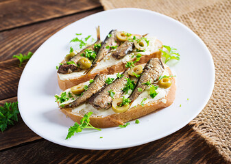 Sandwich - smorrebrod with sprats, green olives and butter on wooden table. Danish cuisine.