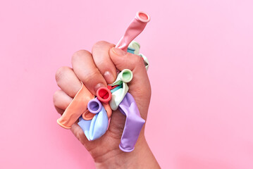 Multicolored not inflated balloons in the hands of a woman on a pink background.