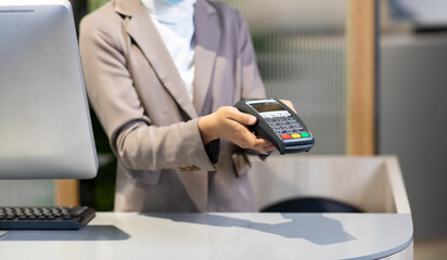 Female receptionist employee holding card reader machine on hand at checkout counter.