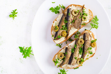 Sandwich - smorrebrod with sprats, green olives and butter on light table. Danish cuisine. Top view, overhead, flat lay