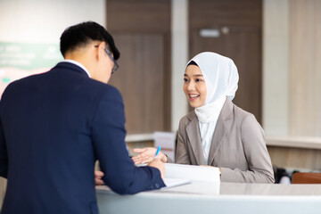Portrait of muslim woman receptionist at desk in lobby.  Asian business man standing at reception desk and talking to muslim woman receptionist.