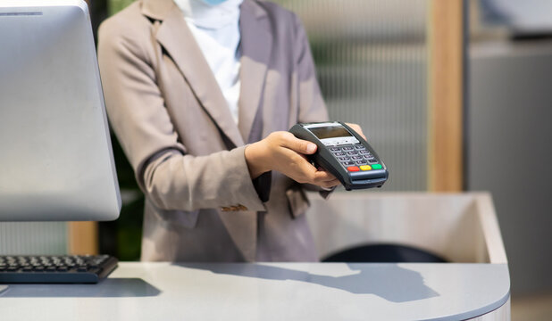 Female receptionist employee holding card reader machine on hand at checkout counter.