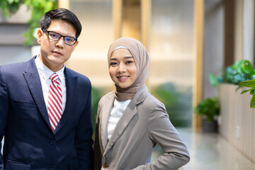 Portrait of young Asian muslim woman wearing hijab head scarf and Asian business man in suite in moder office.