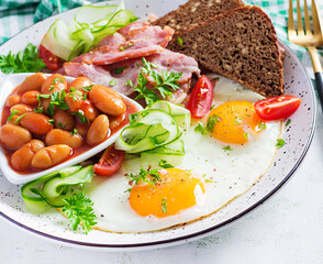 English breakfast - fried egg, beans, bacon, tomatoes  and bread.