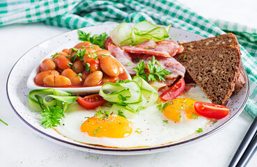 English breakfast - fried egg, beans, bacon, tomatoes  and bread.