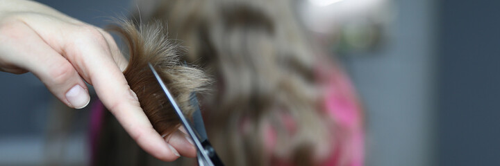 Close-up of mother holding metal scissors and cutting strand of luxury childs hair. Home...