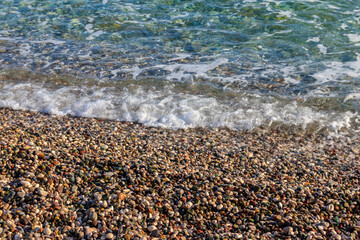 Sea tide on pebble shore of the Mediterranean sea. Waves with white foam on pebble beach