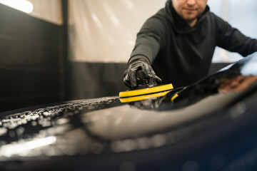 Man cleans rear window of car with  circle sponge. Professional car wash process