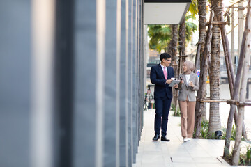 Young business muslim woman and business man colleague walking and discussing outside the office. Woman is holding a coffee and businessman is holding a digital tablet outdoor.