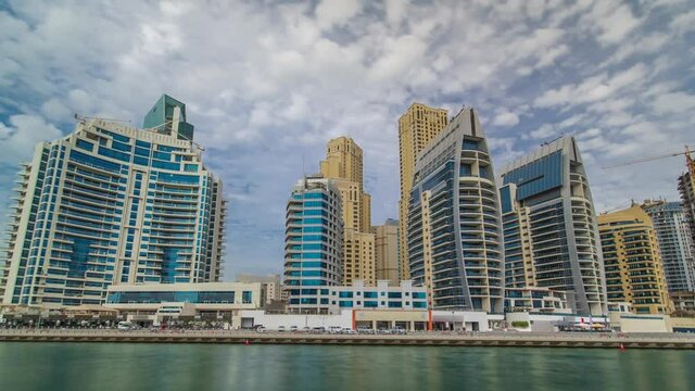 Dubai Marina towers reflected in water from promenade timelapse hyperlapse, United Arab Emirates. Dubai Marina is a district in Dubai and an artificial canal. Blue cloudy sky