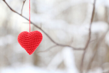 Valentine heart in winter forest. Red knitted symbol of love hanging on a branch, background for holiday