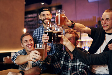 Cheering by knocking beer glasses. Group of people together indoors in the pub have fun at weekend time