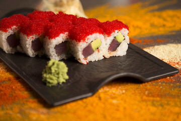Macro of Japanese seafood sushi roll dish with tuna Maguro, avocado. red flying fish roe Tobiko on top served with wasabi, ginger. turmeric, garlic, curry, paprika spices scattered on background
