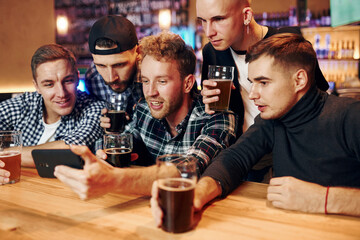 Uses phone. Group of people together indoors in the pub have fun at weekend time