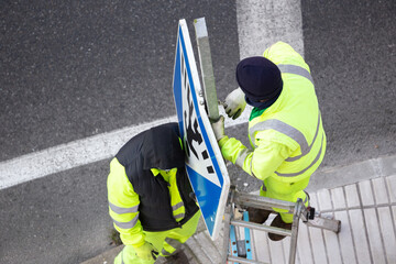 Workers changing a damaged road sign on street sidewalk