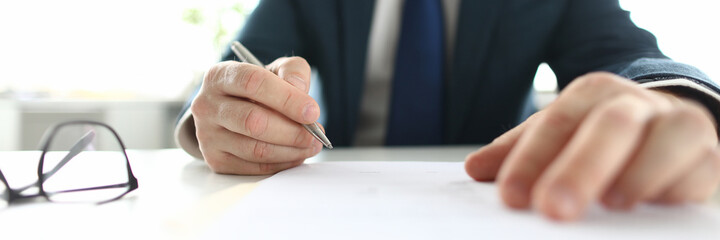 Businessman sits at table holding a pen over document. Business and Political Agreements Concept