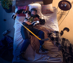 Ready. Top view of young professional hockey player sleeping at his bedroom in sportwear with equipment. Loving his sport, workaholic, playing match even if resting. Action, motion, humor.