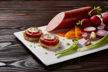 Sausages with a garnish of vegetables and herbs with sauces and bread on a white rectangular plate on a dark wooden table.