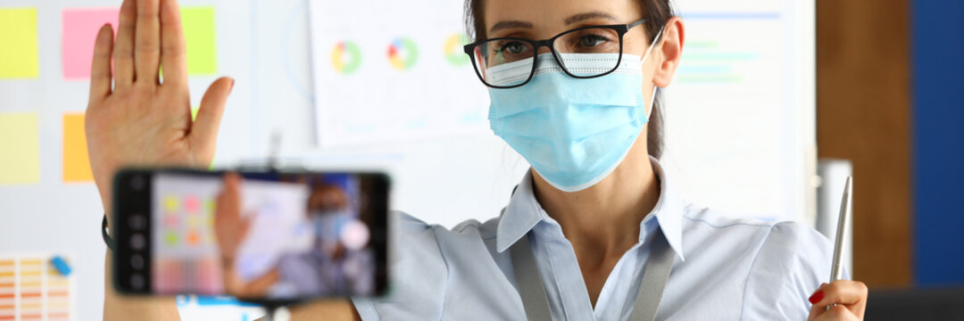 Business blogger in protective medical mask greets interlocutors via a smartphone. Online broadcasting in business concept