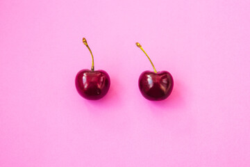 Two ripe cherries on bright neon pink background. Valentine's Day concept. Close-up of cherries. Summer background