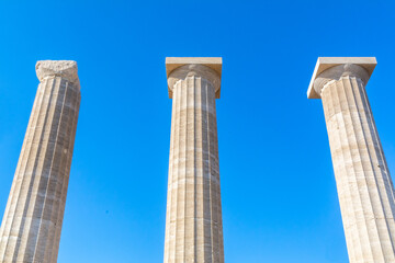ruined columns of the ancient acropolis temple in the greece city lindos on a sunny day with plain...