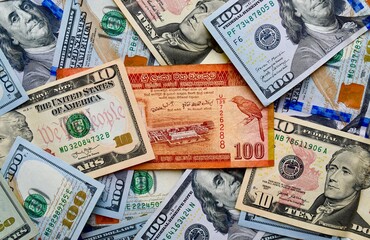 Sri Lankan rupee on top of USA national currency, top view of mixed American dollars banknotes. LKR...