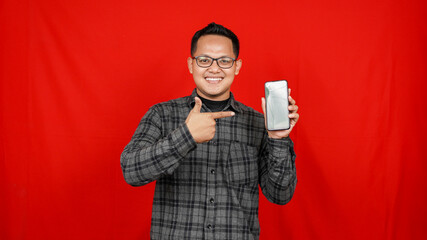 Funny Asian man pointing handphone isolated red background