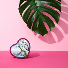Pink background with a tropical leaf and object in the heart shape with a photo of nature